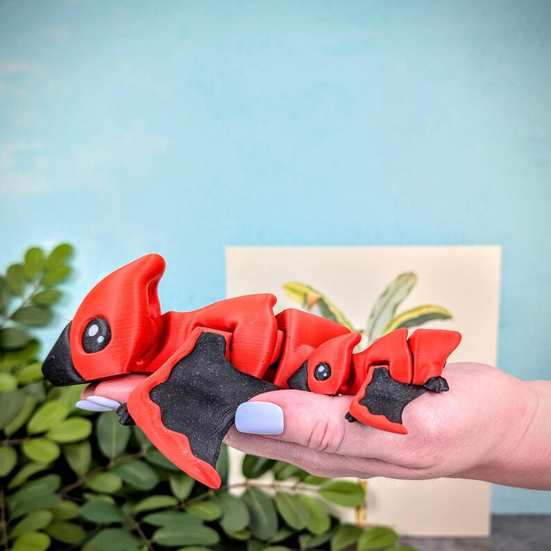 May include: A set of three red and black articulated dinosaur toys. The dinosaurs are posed in a walking position with their heads tilted up.