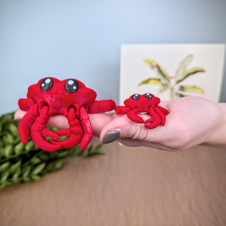May include: Two red plastic toy crabs with googly eyes. The larger crab is holding its claws together. The smaller crab is standing with its claws out.
