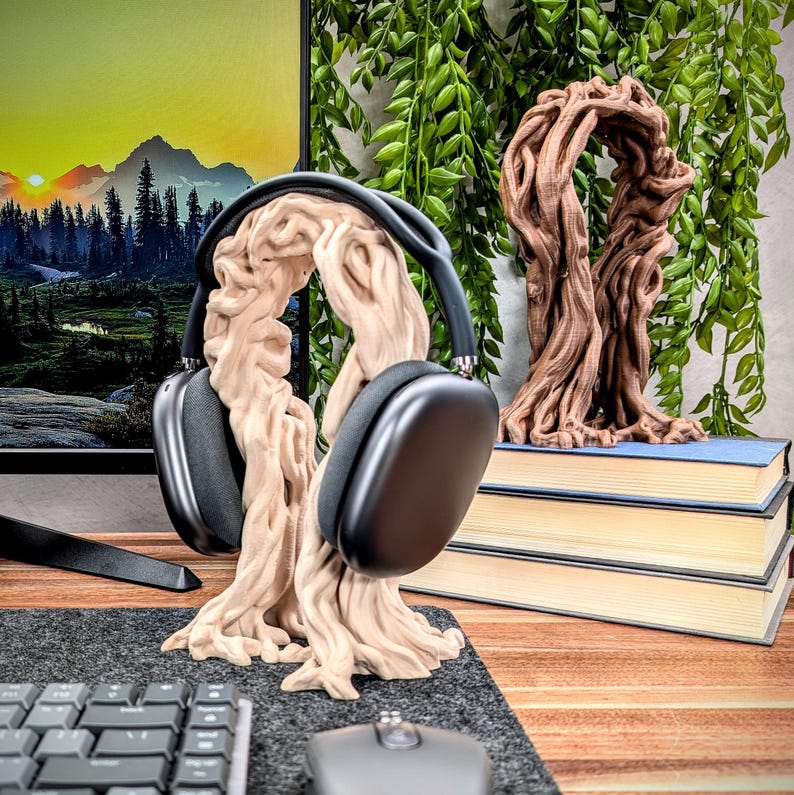 May include: A wooden headphone stand shaped like a tree with a pair of black headphones resting on the branches. The stand is on a desk with a keyboard and mouse.