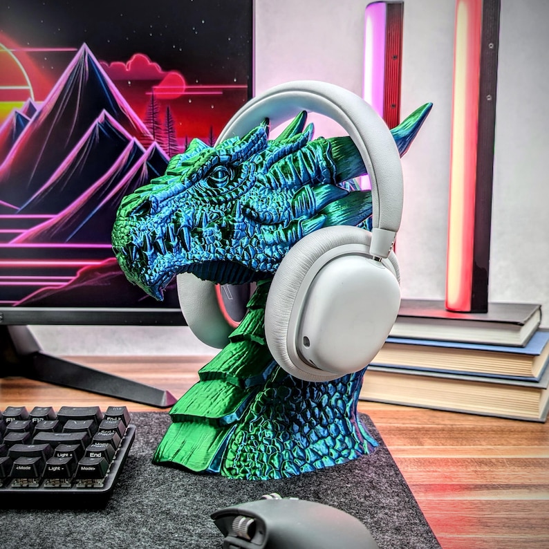 May include: A green and blue dragon head headphone stand. The dragon's head is facing to the left and has a white pair of headphones resting on its head.