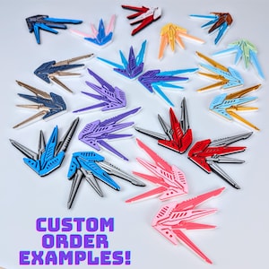 May include: A collection of custom order examples featuring various colorful, geometric designs. The designs are in shades of blue, purple, red, pink, gold, and silver. The text "CUSTOM ORDER EXAMPLES!" is displayed in a vibrant, multi-colored font.