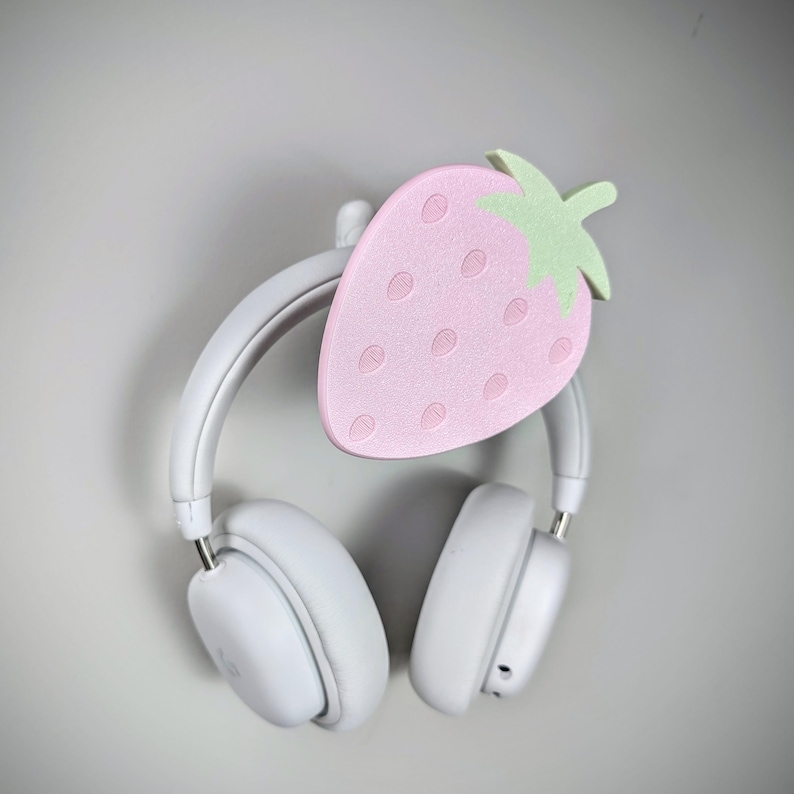 May include: White headphones with a pink and green strawberry-shaped headphone stand.