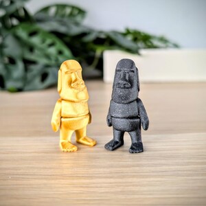 May include: Two small statues of a person with a large nose and large ears. One statue is gold and the other is black.