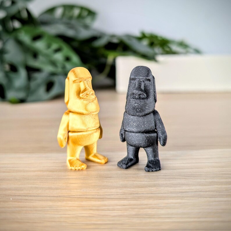 May include: Two small statues of a person with a large nose and large ears. One statue is gold and the other is black.
