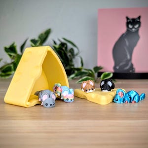 May include: A set of five small mouse figurines, each with a different color and design. The figurines are arranged on a yellow cheese-shaped container and a yellow cheese-shaped tray.