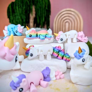 May include: A collection of colorful, articulated unicorn figurines. Each unicorn is made of plastic and has a different color scheme. The unicorns are posed in various positions, some standing, some lying down, and some sitting. The figurines are all about 3 inches tall.