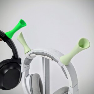 May include: A white and gray headset with light green accessories. A black headset with a light green accessory is also visible. The accessories are shaped like horns and are attached to the headsets.