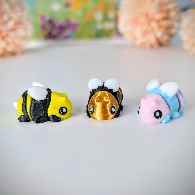 May include: Three small bee figurines, one is yellow and black, one is gold, and one is light blue and pink.