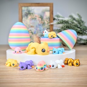 May include: A collection of colorful, handmade figurines, including chicks, birds, and an Easter egg. The figurines are in various colors, including yellow, purple, pink, and blue. The Easter egg is striped with pastel colors. The figurines are displayed on a white platform.