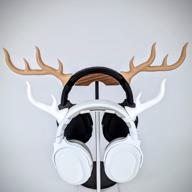 May include: A white headset with a black headband is displayed on a wooden stand with two antlers. The stand is made of wood and has a brown finish.