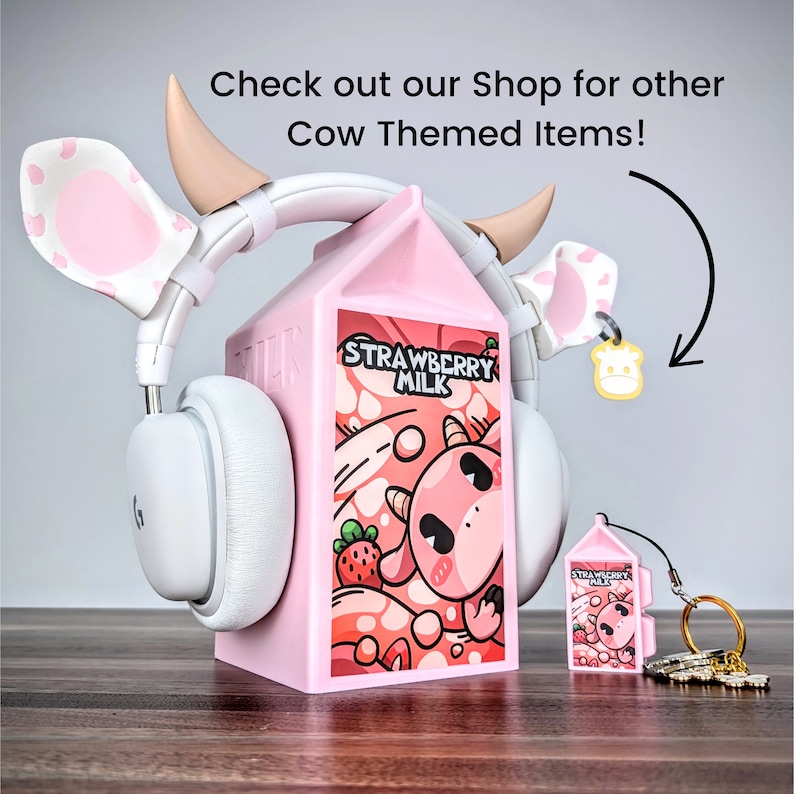May include: Pink cow-themed headphones with a pink milk carton stand. The milk carton has a cartoon cow and the words "Strawberry Milk" on it. There is a smaller pink milk carton keychain with a cow on it.