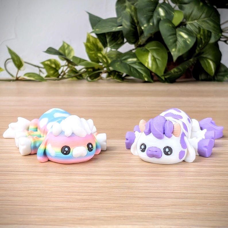 May include: Two small, colorful, hand-painted figurines. One is a rainbow-colored creature with a white fluffy head. The other is a white creature with purple spots and a purple mane. Both have large, black eyes.