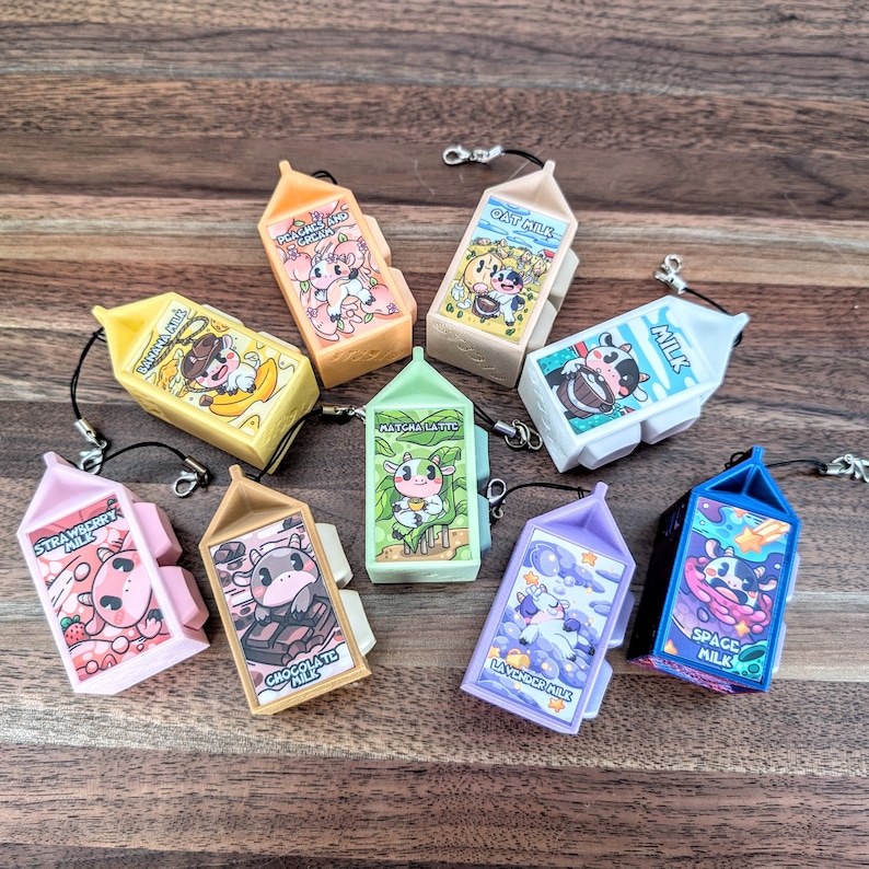 May include: Nine colourful miniature milk carton keychains with different flavours and designs. Each keychain features a cartoon cow and the name of the flavour. The flavours include Strawberry, Chocolate, Matcha Latte, Oat Milk, Peach & Cream, Space Milk, and La Vendor Milk.