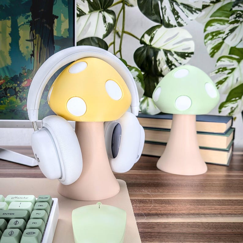 May include: A yellow mushroom-shaped headphone stand with white polka dots and a white headset. A green mushroom-shaped stand with white polka dots is in the background.