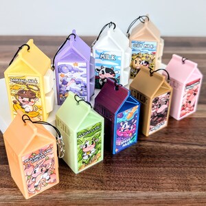 May include: A collection of ten colourful milk carton-shaped keychains with different animal and text designs. The keychains feature designs such as "Banana Milk", "Oat Milk", "Space Milk", "Matcha Latte", and "Peaches and Cream".