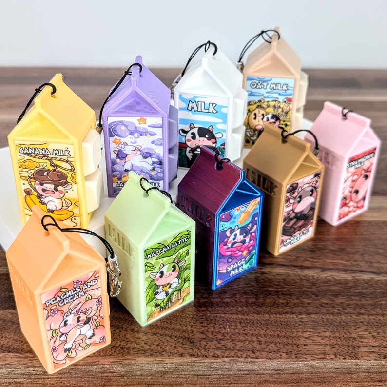 May include: A collection of ten colourful milk carton-shaped keychains with different animal and text designs. The keychains feature designs such as "Banana Milk", "Oat Milk", "Space Milk", "Matcha Latte", and "Peaches and Cream".