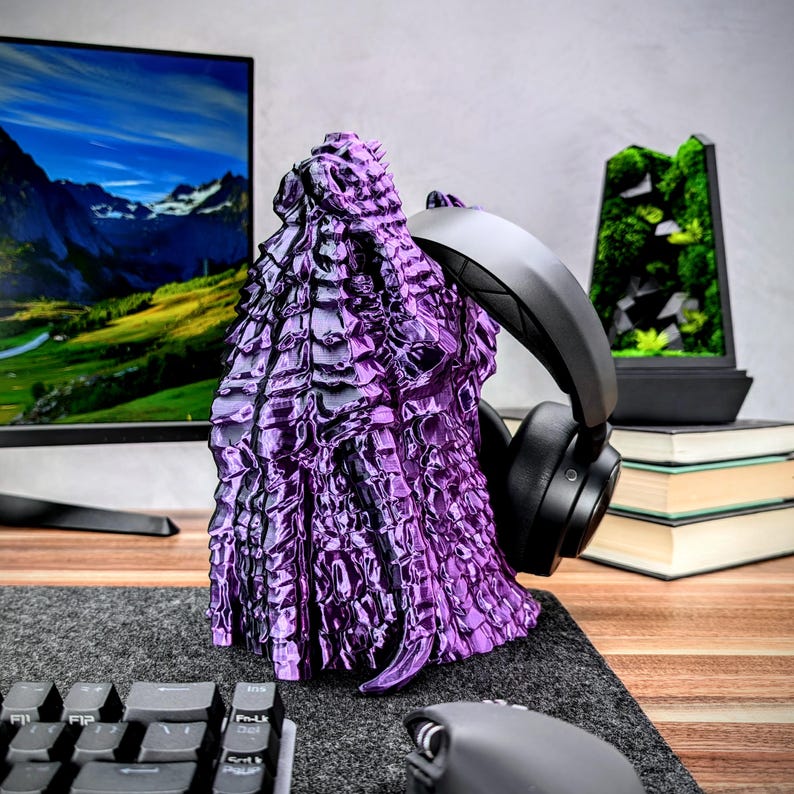 May include: A purple and black 3D printed dragon head headphone stand. The stand is on a wooden desk with a keyboard and mouse.