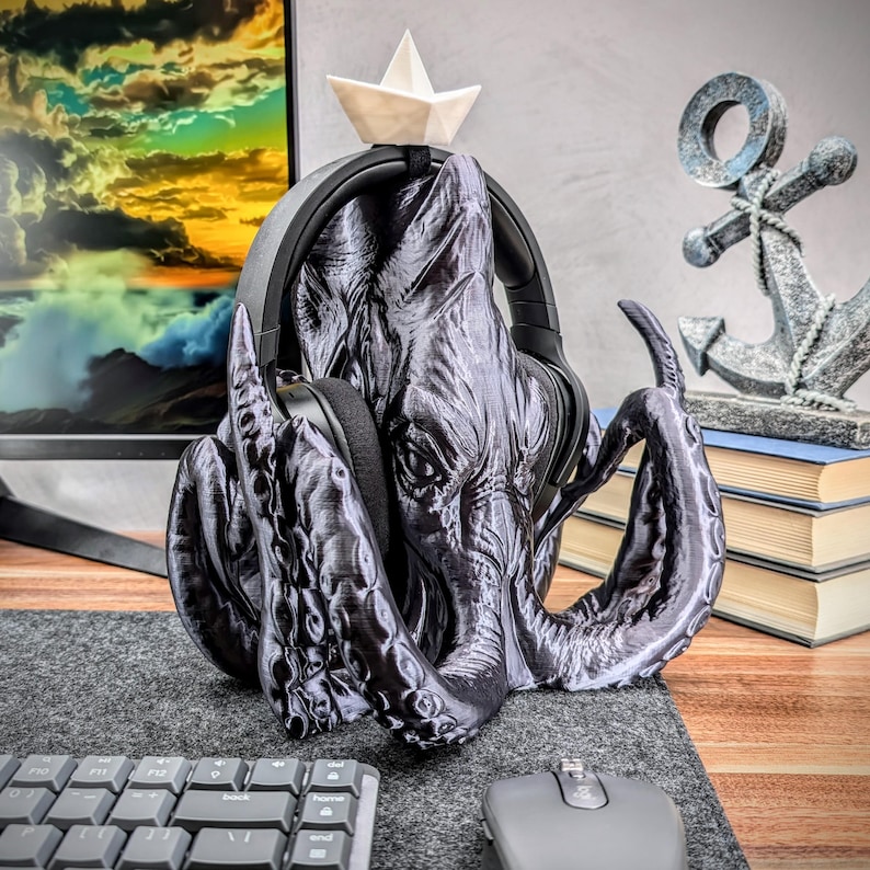 May include: A black 3D printed octopus headphone stand with a small white paper boat on top. The stand is holding a pair of black headphones.