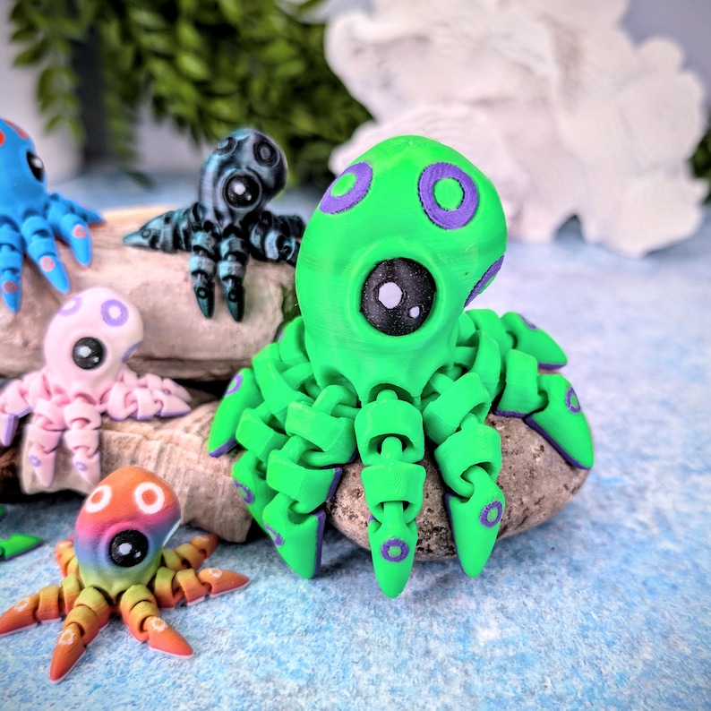 May include: A bright green octopus figurine with purple accents and large, white eyes. The octopus is sitting on a gray rock.