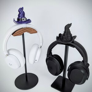 May include: Two black and white headphones with stands. The stands are decorated with witch hats. The white headphones have a wooden base and the black headphones have a metal base.