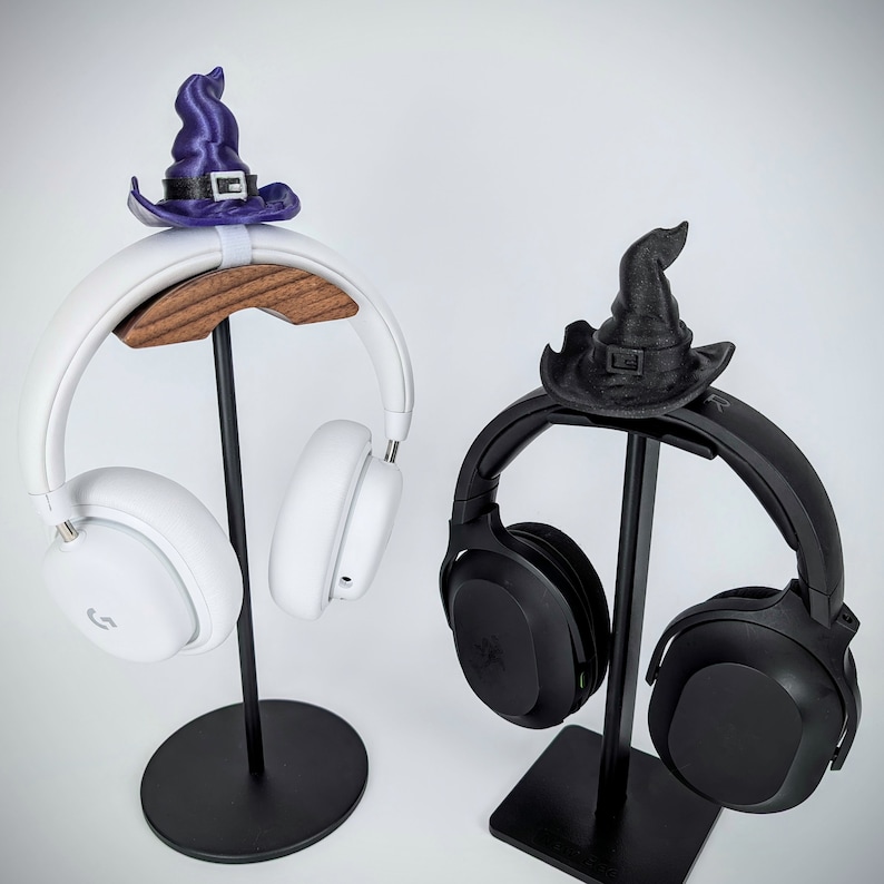 May include: Two black and white headphones with stands. The stands are decorated with witch hats. The white headphones have a wooden base and the black headphones have a metal base.