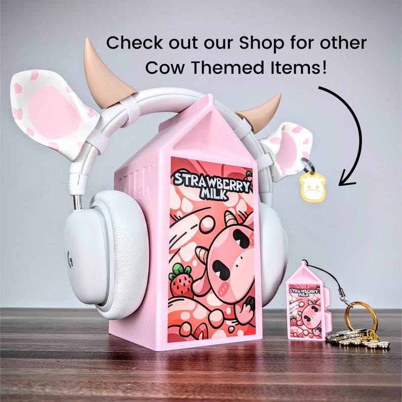 May include: Pink cow-themed headphones with a pink milk carton stand. The milk carton has a cartoon cow and the words "Strawberry Milk" on it. There is a smaller pink milk carton keyring with a cow on it.