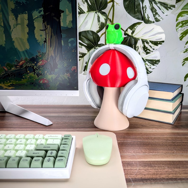 May include: White headphones with a red and white mushroom-shaped stand. A green frog figurine sits on top of the mushroom. The stand is on a wooden desk with a keyboard and a mouse.