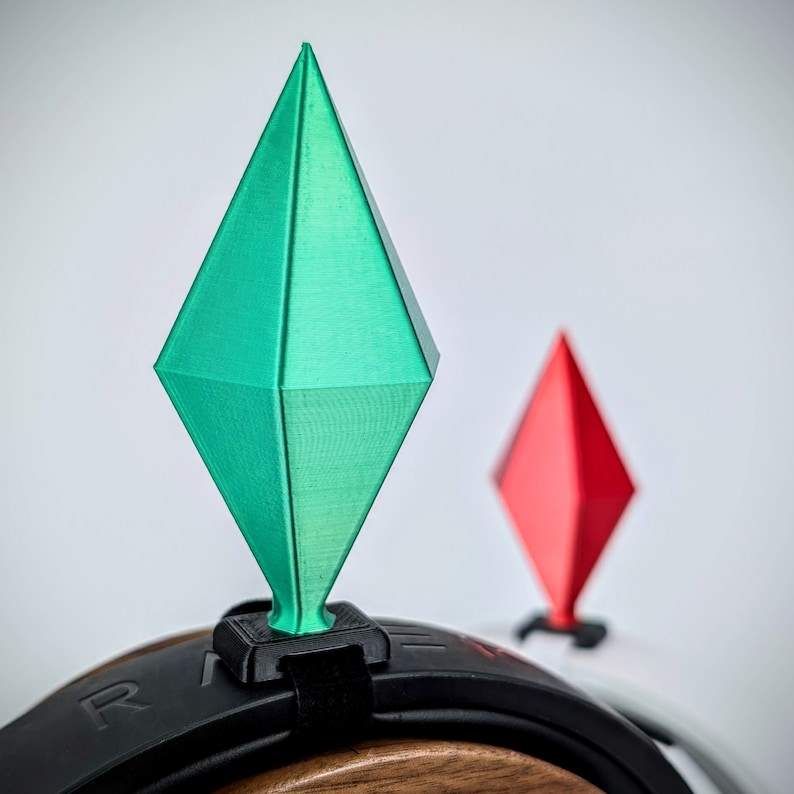 May include: A green and red 3D printed diamond-shaped object attached to a black headband. The headband is made of a soft, flexible material and has a black strap.