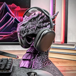 May include: A purple dragon-shaped headset stand with a black headset resting on it. The stand is made of 3D printed plastic and has a detailed dragon design.