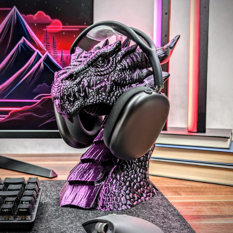 May include: A purple dragon-shaped headset stand with a black headset resting on it. The stand is made of 3D printed plastic and has a detailed dragon design.