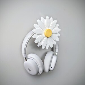 May include: White headphones hanging on a white daisy-shaped headphone holder with a yellow center.