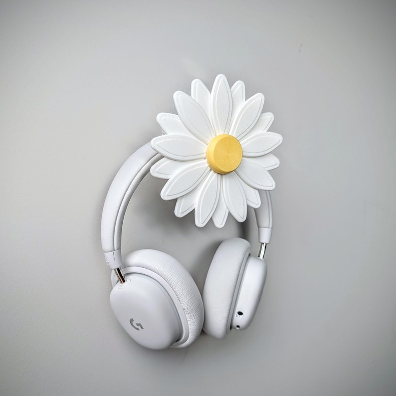 May include: White headphones hanging on a white daisy-shaped headphone holder with a yellow center.