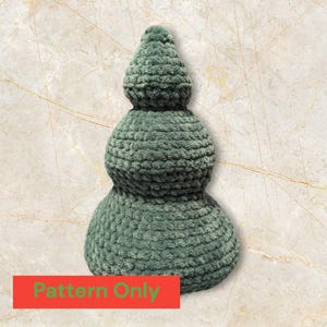 May include: A green crocheted Christmas tree ornament with three tiers. The ornament is made of a soft, fuzzy yarn and has a rounded, bulbous shape. The text "Pattern Only" is visible at the bottom of the image.