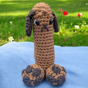 May include: A brown crocheted dog toy with black spots. The toy has large, black eyes and a brown nose.
