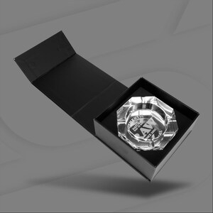 May include: A clear, faceted glass ashtray with the text "AUTHENTIC RAW THE NATURAL WAY TO ROLL SINCE 2005" inside a black box. The ashtray is in a black presentation box with a magnetic closure.