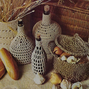 Op de afbeelding: Gebreide hoezen voor flessen en een mand met uien en knoflook. De hoezen zijn gemaakt van beige garen en hebben een delicaat, opengewerkt ontwerp. De mand is ook gebreid en heeft een deksel.