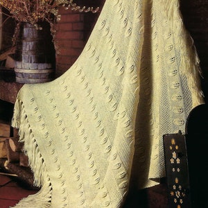 Könnte beinhalten: Eine weiße Häkeldecke mit einem Blatt-Muster und Fransen. Die Decke ist über eine Holzoberfläche gelegt.