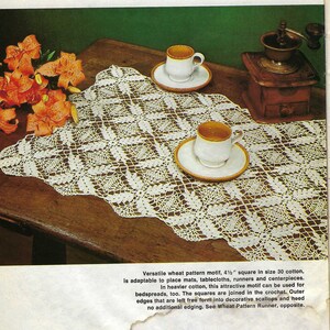 Peut inclure: Un chemin de table en crochet blanc avec un motif de blé. Le chemin de table mesure 11,4 cm de côté et est réalisé en coton taille 30. Le chemin de table est présenté sur une table en bois avec deux tasses de café et une moulinette à café.