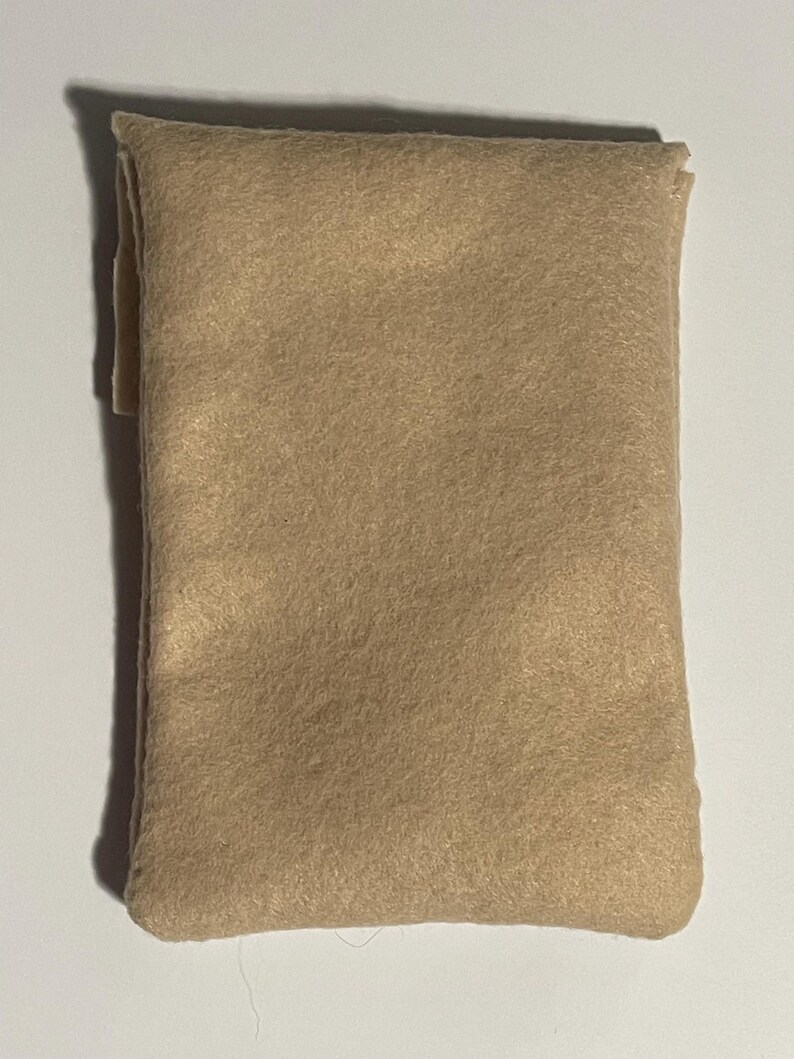 Puede incluir: Una funda rectangular y plegada de fieltro color beige. La funda est&aacute; hecha de un material suave y texturizado y parece estar vac&iacute;a. Los bordes est&aacute;n cuidadosamente cosidos y el dise&ntilde;o es simple y minimalista.