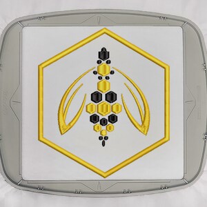 Könnte beinhalten: Ein goldener sechseckiger Rahmen mit einem stilisierten schwarzen und goldenen Bienendesign im Inneren. Die Biene besteht aus Wabenformen.