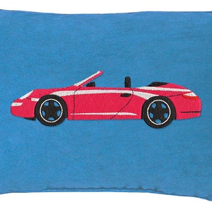 May include: A rectangular blue pillow with a red convertible car embroidered on it. The car has white stripes and black wheels. The pillow is a solid blue color.