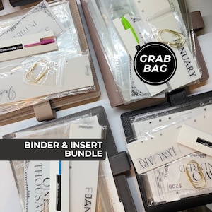 May include: Four planners in beige, brown, gray, and black with textured covers. Each contains clear plastic pouches holding paper inserts, gold-toned paper clips, and pens in various colors. Text on inserts includes January, Two Hundred, and One Thousand.