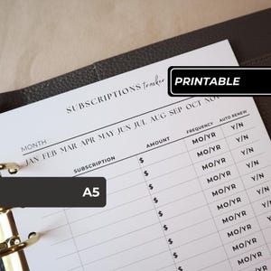 May include: A white A5 paper subscription tracker insert with black text and lines. The header reads SUBSCRIPTIONS tracker. Columns include Month, Subscription, Amount, Frequency, and Auto Renew with Y/N options. Gold metal binder rings are visible.