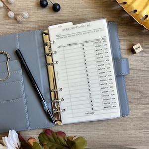 May include: A clear plastic sheet with a subscription tracker for bills. The sheet has columns for month, due date, subscription, amount, frequency, and auto renew. The sheet is designed to be used in a binder.