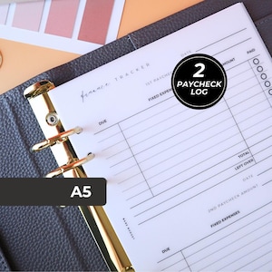 May include: A5 size finance tracker planner with gold-colored rings. The planner is open to a page labeled "Paycheck Log" with spaces for dates, amounts, and expenses. The planner is gray with a light-colored background.