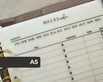 Puede incluir: Una hoja de seguimiento de facturas A5 translúcida con texto y líneas impresas en negro. El encabezado dice BILLS tracker, seguido de los meses de JAN a DEC. Las columnas incluyen BILL, AMOUNT con signos de dólar, DUE y PAID, sujeta por anillas doradas.