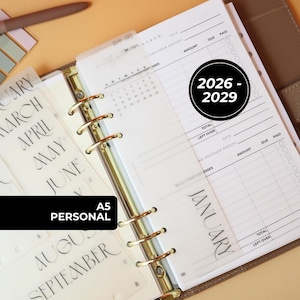 May include: A ring-bound planner with white pages featuring a monthly bill tracker, a calendar for January 2027, and translucent dividers labeled with months. The planner includes a black circular graphic with the text 2026 - 2029 and A5 PERSONAL.