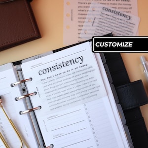 May include: A ring-bound planner featuring a translucent dashboard with the text consistency and a motivational paragraph. The page includes a section for week priorities, Wednesday, and Thursday, with a gold metal paperclip and a black cover.