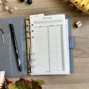 May include: A white page with a bills tracker for a personal planner. The page has columns for month, bill, amount, due, and paid. There are checkboxes for paid.