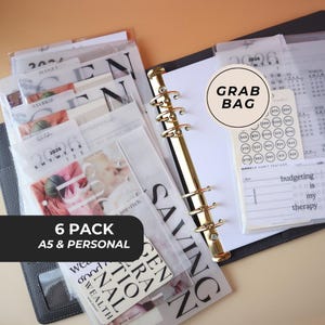 May include: A black A5 & Personal planner with gold rings, filled with inserts. The inserts include budgeting, savings, and habit tracker pages. The image also shows a "Grab Bag" label and the text "6 Pack A5 & Personal".